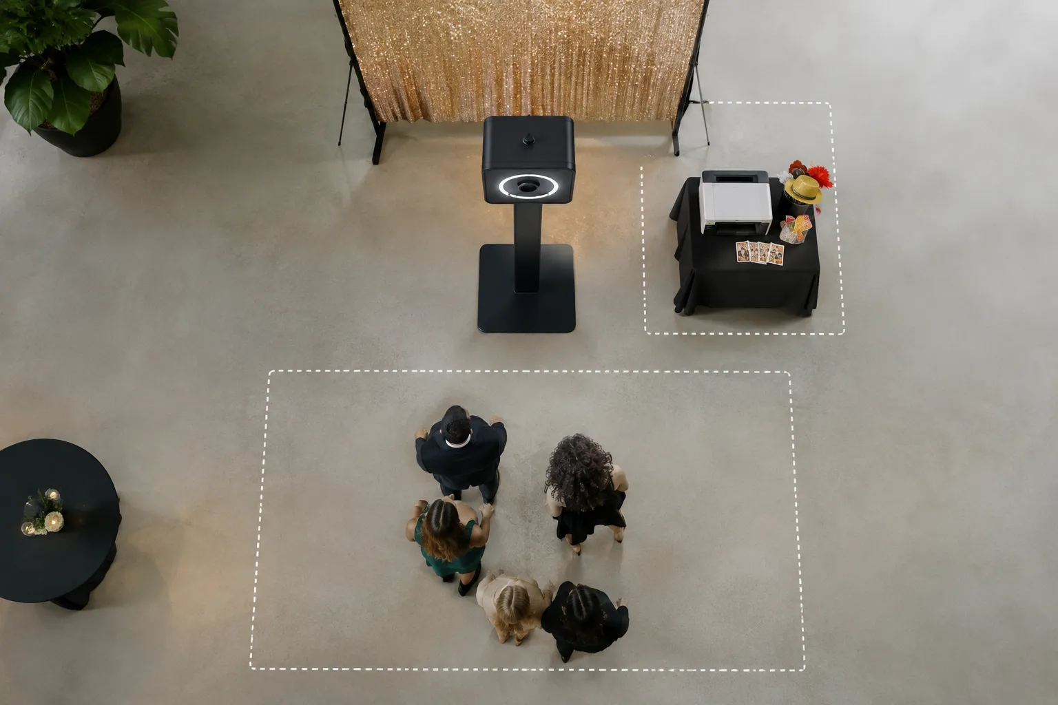 Open fotobooth met gouden achtergrond, printertafel en vijf gasten binnen een gestippelde vloerzone